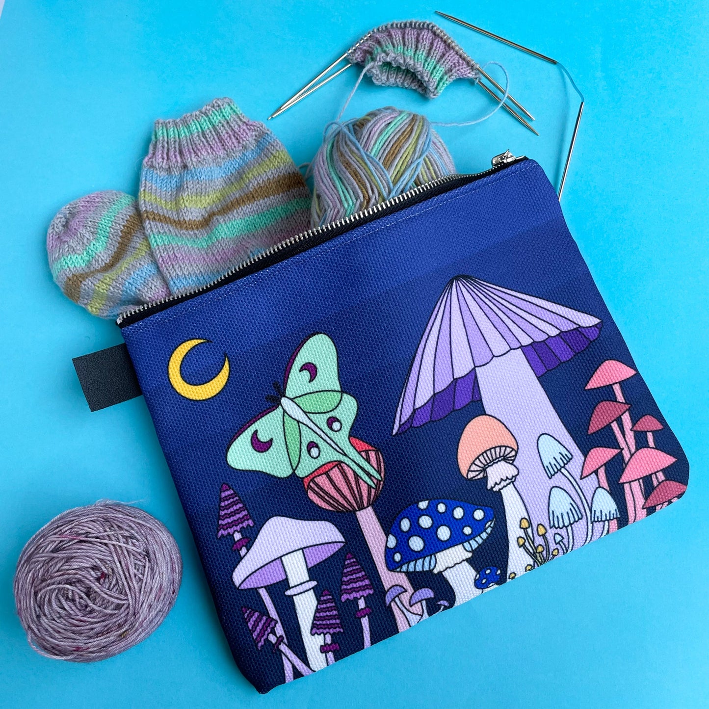 A bag with a scene of pastel mushrooms on it with an in progress sock project coming out of the bag.