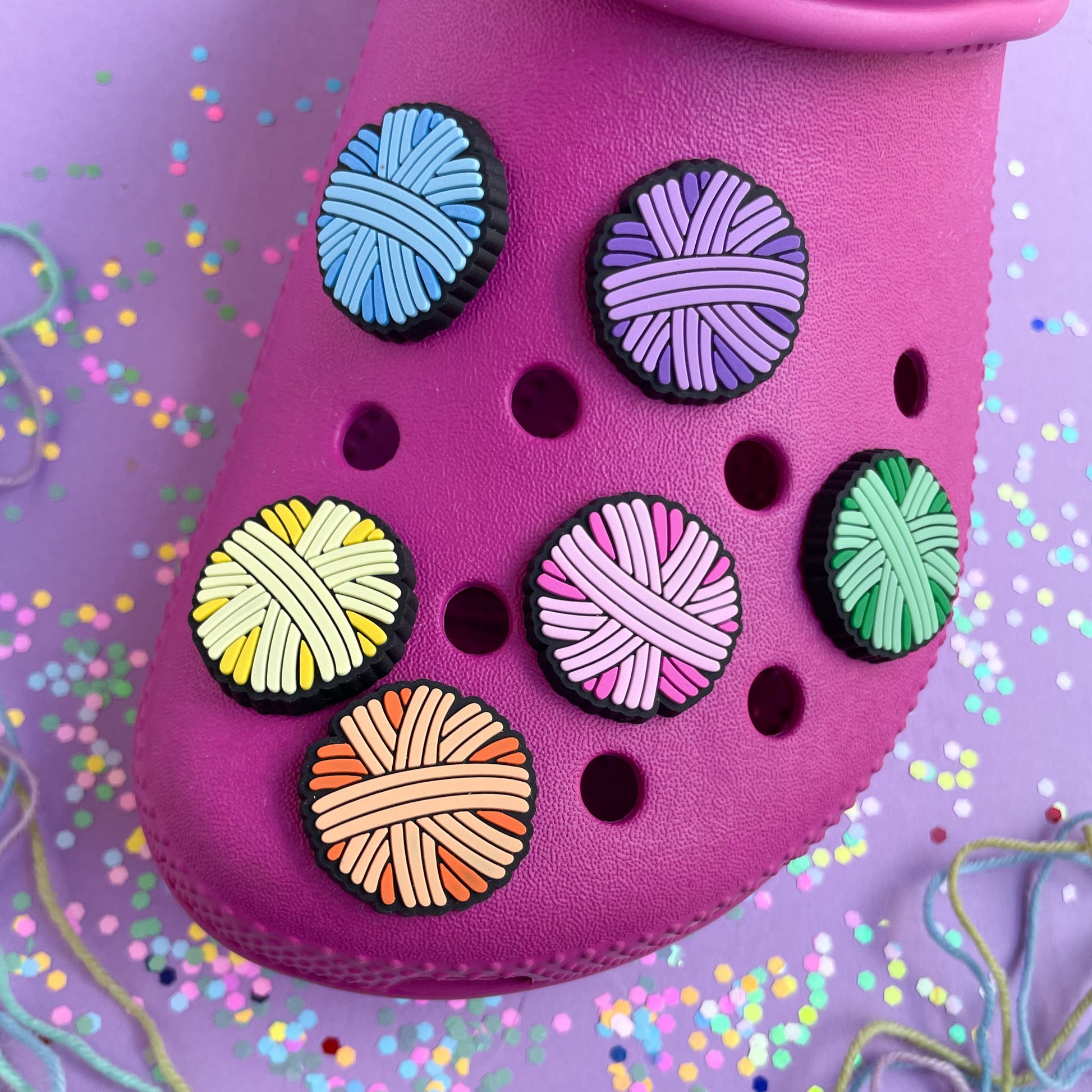A hot pink shoe with pastel rainbow yarn ball charms on it. 